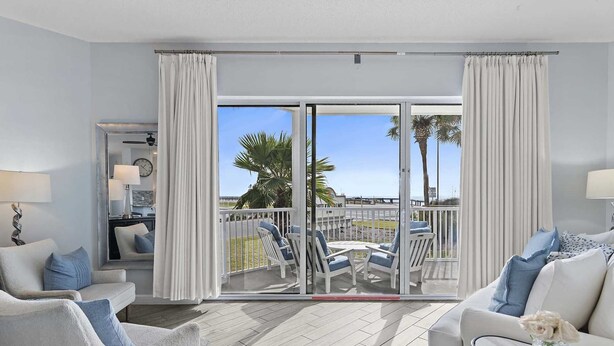 A modern hotel room with a balcony, white furniture, and a view of the beach. - Guest Favorite| Gulf Front | Accommodates 12 |  Beach Serv. I Pet Friendly| (Miramar Beach)