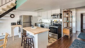 A modern kitchen with a central island, stainless steel appliances, and a staircase leading to an upper level. - Gearhart House G748 (Gearhart)