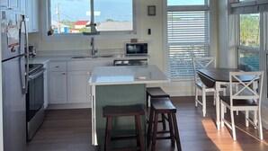 A modern kitchen with white cabinets, a central island, a ceiling fan, and a view of the outside.