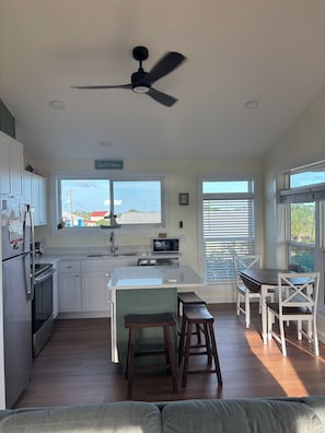 A modern kitchen with white cabinets, a central island, a ceiling fan, and a view of the outside.