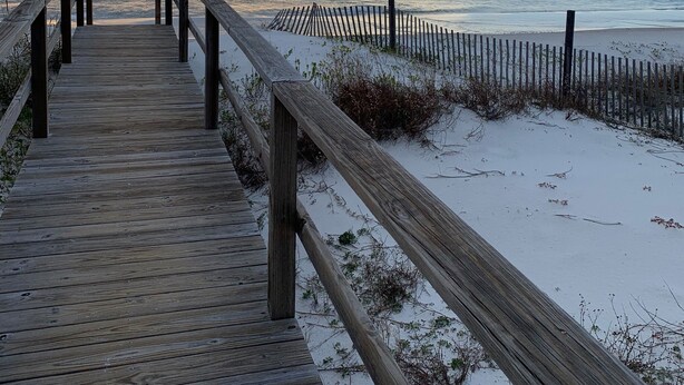 A wooden boardwalk leading to a beach with a sandy shoreline and a wooden fence.