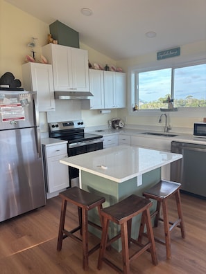 A modern kitchen with white cabinets, a stainless steel refrigerator, a stove, and a large island with stools. - Cape San Blas North End Gulf view from large porch.   (Cape San Blas)