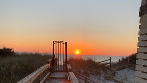 A wooden boardwalk leading to a gated entrance with a sunset in the background.