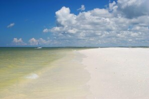 A beach with clear water, a boat in the distance, and a cloudy sky. - Almost Beachfront for Less -Ocean & Sunset Views-Near JW Marriott (MARCO ISLAND)