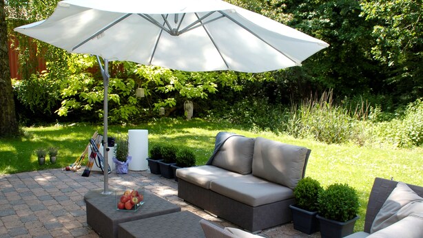 An outdoor patio with a gray sofa, a white umbrella, and potted plants. - Hotel Auszeit (Isernhagen)