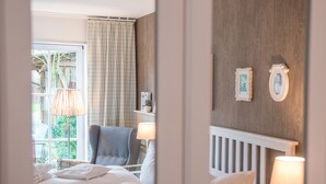 A bedroom with a bed, a chair, a lamp, and a window with curtains. - Hotel Auszeit (Isernhagen)