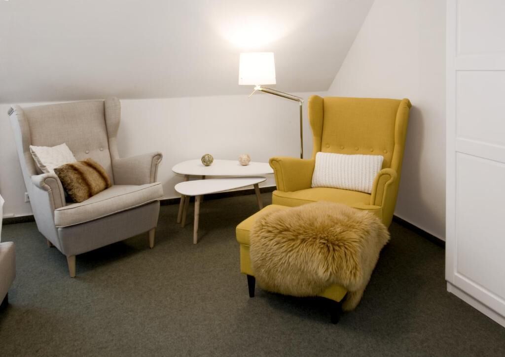 A cozy room with a grey armchair, a yellow armchair with a fur throw, and a small white table with decorative items.