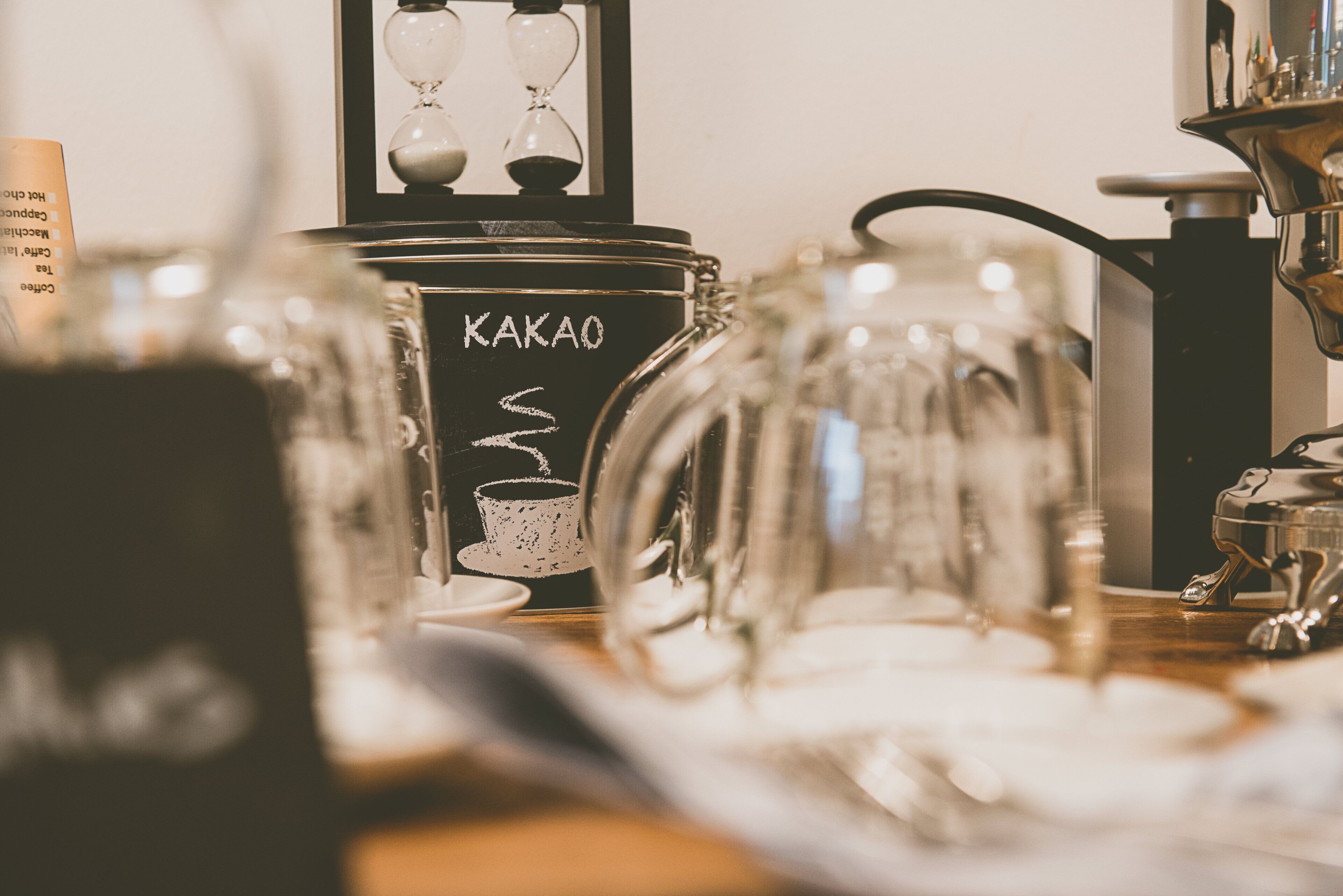 Interior de una cafetería con énfasis en una máquina de café y cristalería de marca KAKAO.