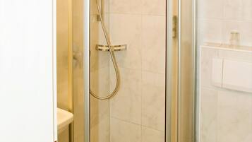 Una ducha en esquina con puerta de cristal, un inodoro blanco y suelo de baldosas de mármol.