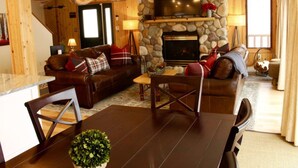 A cozy living room with a stone fireplace, leather sofas, and a dining area with a table and chairs.