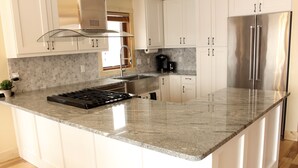 A kitchen with white cabinets, a stainless steel refrigerator, a gas stove, and a coffee maker.