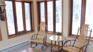 A room with three rocking chairs, a small table, and a potted plant.