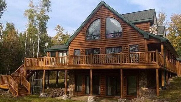 A log cabin with a balcony, a staircase, and a stone foundation.
