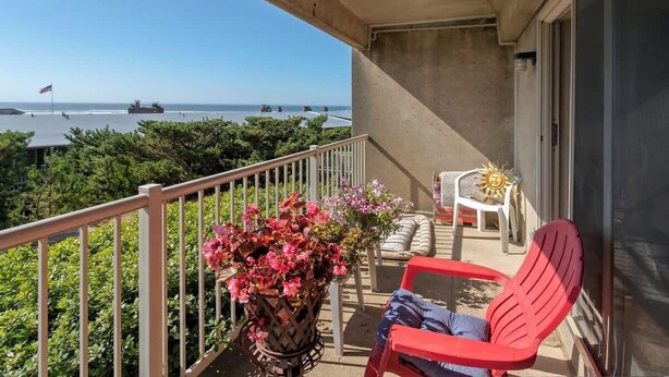 A balcony with a view of the sea, a potted plant, and red chairs. - Gearhart House G613 (Gearhart)