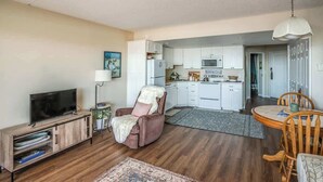 A living room with a TV, a sofa, a dining table with chairs, and a kitchen in the background. - Gearhart House G613 (Gearhart)