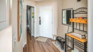 A hallway with a white door, a wooden floor, a metal bench with a tray, and a wall-mounted mirror. - Gearhart House G613 (Gearhart)