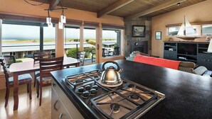 Une cuisine moderne dotée d’un grand îlot central, d’un coin repas avec une table et des chaises, et offrant une vue sur l’extérieur.