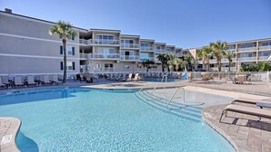 A swimming pool with lounge chairs and palm trees, surrounded by a multi-story building with balconies. - Beachfront Condo 322, Luxury 1 BR at Beachside Colony NEW POOL (Tybee Island)