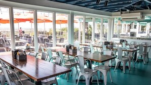 A restaurant with outdoor seating, large windows, and a teal-colored floor. - Beachfront Condo 322, Luxury 1 BR at Beachside Colony NEW POOL (Tybee Island)
