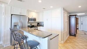 A modern kitchen with white cabinetry, a granite countertop, and stainless steel appliances. - Beachfront Condo 322, Luxury 1 BR at Beachside Colony NEW POOL (Tybee Island)