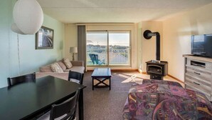 Una habitación con una mesa de comedor, un sofá, una cama estampada, un televisor y vistas de un paisaje urbano a través de un ventanal grande.