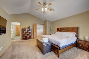 Quarto com uma cama grande, cabeceira de madeira, mesa de cabeceira, penteadeira, ventoinha no teto e piso coberto por carpete.