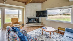 A spacious living room with a fireplace, large windows, and a view of the landscape. - Pacific Terrace T401 (Gearhart)