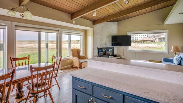 A spacious kitchen with a large island, wooden ceiling beams, and a view of the outdoors. - Pacific Terrace T401 (Gearhart)