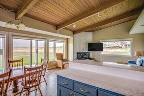 A spacious kitchen with a large island, wooden ceiling beams, and a view of the outdoors. - Pacific Terrace T401 (Gearhart)