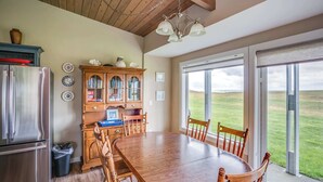 A kitchen with a wooden table, chairs, a refrigerator, and a view of the outdoors. - Pacific Terrace T401 (Gearhart)