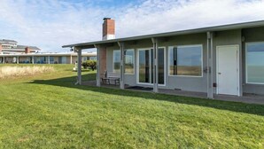 A building with a covered patio, a brick chimney, and a grassy lawn. - Pacific Terrace T401 (Gearhart)