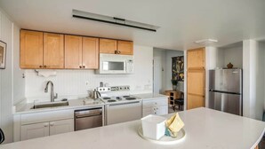 Una cocina moderna con armarios de madera, una encimera blanca, un refrigerador de acero inoxidable y un microondas.