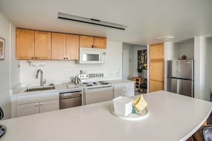 A modern kitchen with wooden cabinets, a white countertop, a stainless steel refrigerator, and a microwave. - Gearhart House G665 (Gearhart)