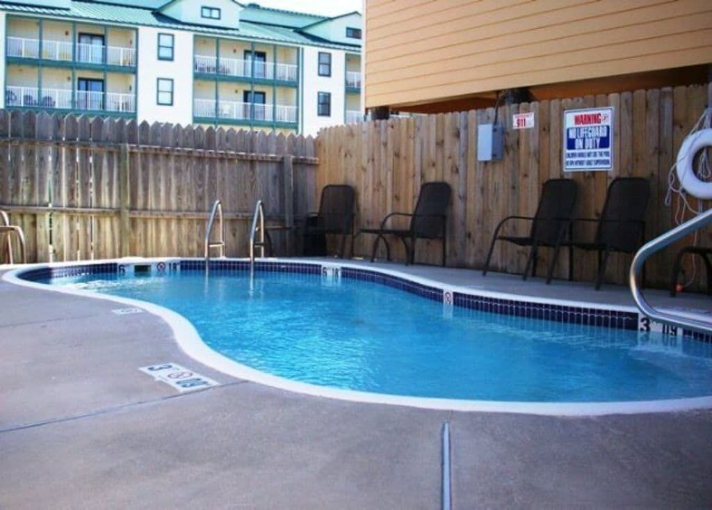 A swimming pool with a wooden fence, lounge chairs, and a lifeguard sign.