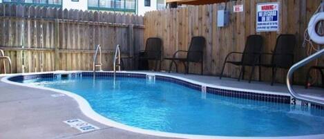 A swimming pool with a wooden fence, lounge chairs, and a lifeguard sign.