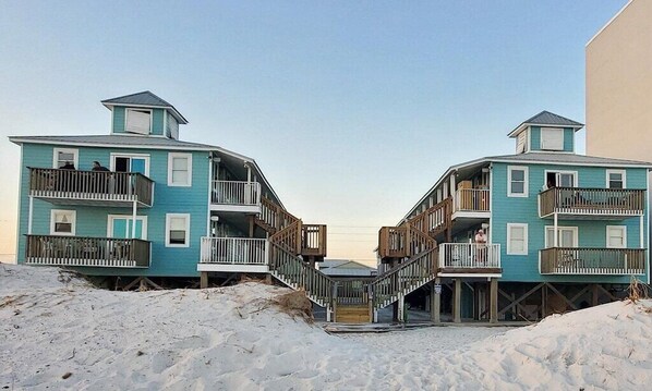 A beachfront property with two multi-story buildings featuring balconies and wooden staircases.