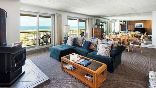 Ein Wohnzimmer mit Sofa, Couchtisch und Kamin. Ein Balkon bietet Blick auf das Meer.