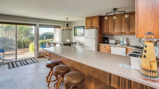 A modern kitchen with a large island, wooden cabinets, and a view to the outside.
