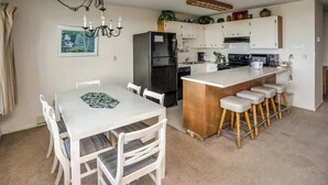 A modern kitchen with white cabinetry, a central island with stools, a black refrigerator, and a chandelier. - Pacific View V473 (Gearhart)