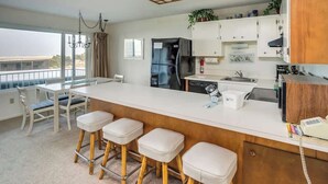 A modern kitchen with a central island, bar stools, a refrigerator, and a view of the outdoors. - Pacific View V473 (Gearhart)