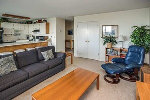 A living room with a sofa, coffee table, and a blue leather chair. - Pacific View V473 (Gearhart)
