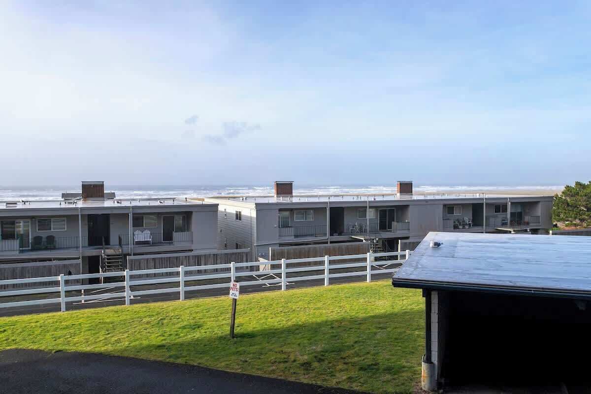 A row of modern, single-story buildings with a white fence in front, overlooking a beach.