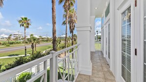 A balcony with a view of a road and palm trees, white railings, and a tiled floor. - Incredible Beach House with Pool! Short safe walk to the beach, Family Area (South Padre Island)