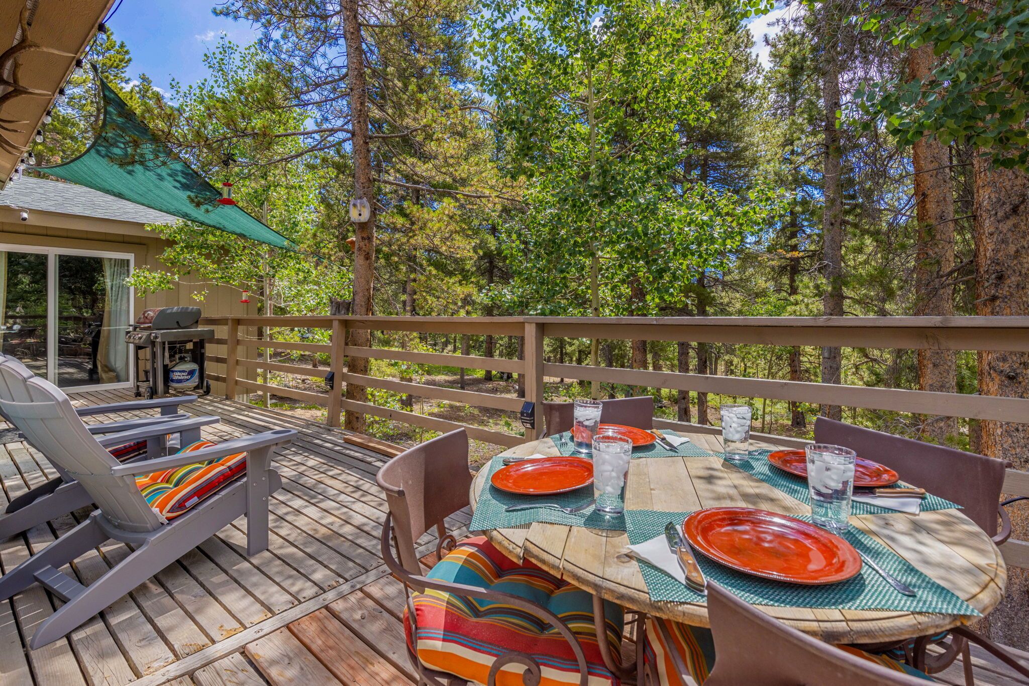 Une terrasse en bois avec une table dressée pour le repas, entourée de chaises et abritée par une zone couverte.
