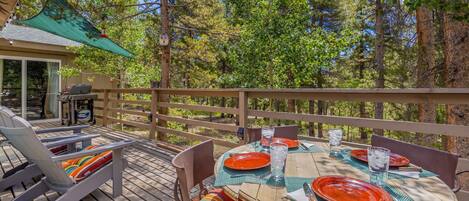 Une terrasse en bois avec une table dressée pour le repas, entourée de chaises et abritée par une zone couverte.