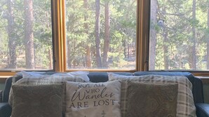 Una cama con una colcha escocesa y tres almohadones decorativos, uno con un paisaje forestal y texto.