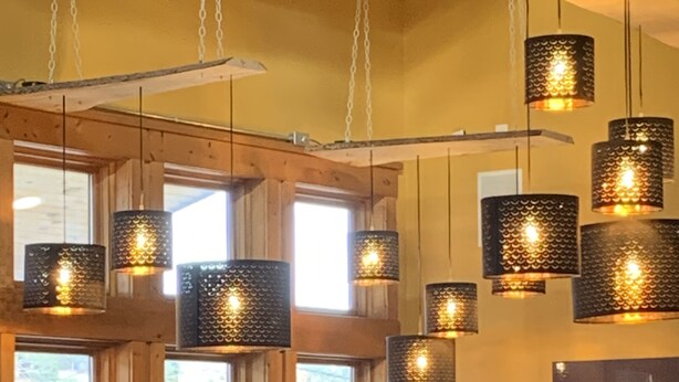 Un interior de restaurante con lámparas colgantes, vigas de madera y un ventanal grande.