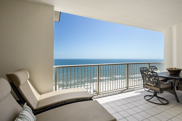 A balcony with a view of the ocean, a table with chairs, and a sofa.