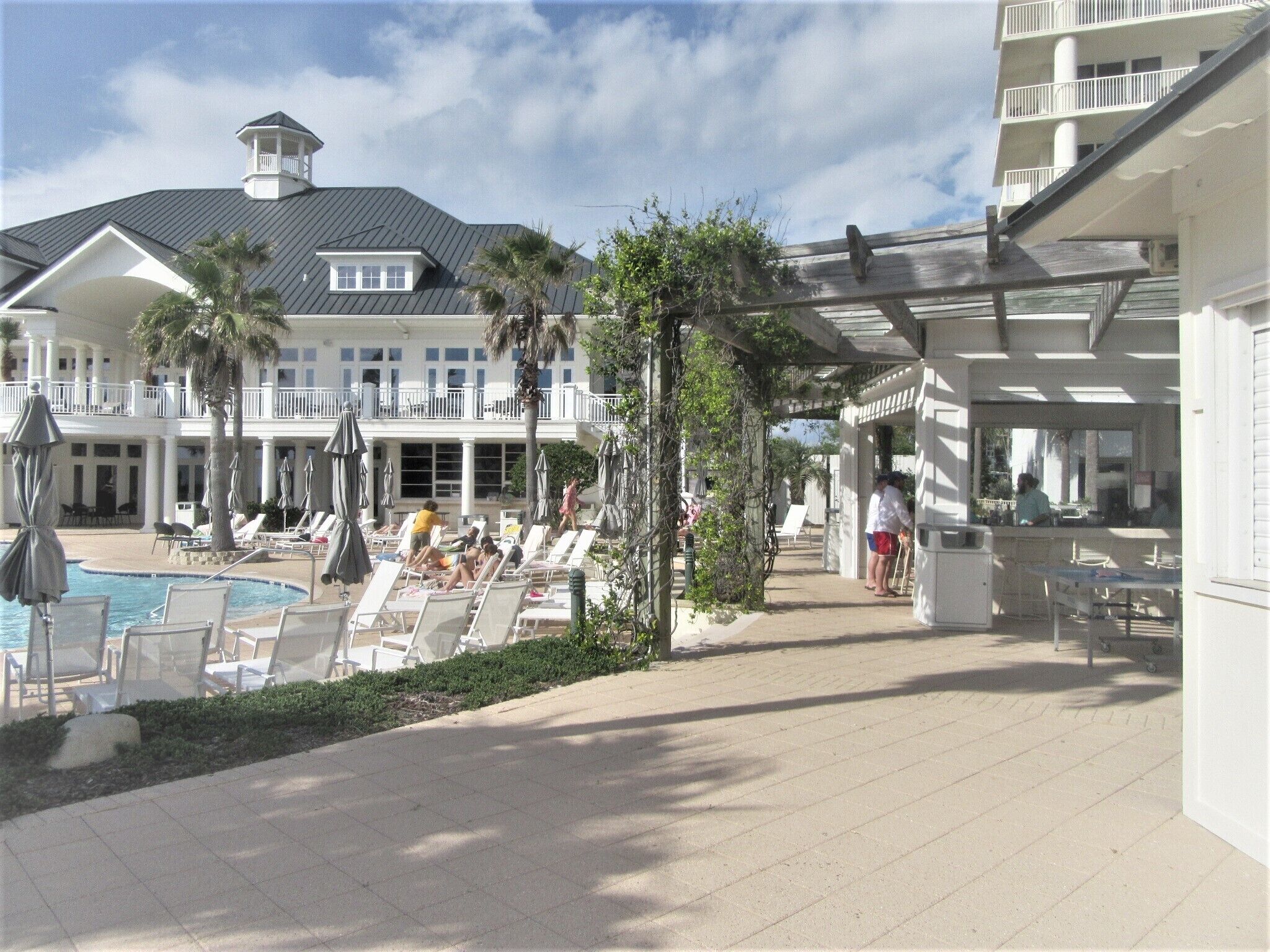 A resort pool area with lounge chairs, umbrellas, and a building with a balcony.