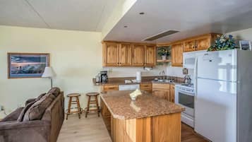 A kitchen with wooden cabinets, a granite countertop, a refrigerator, and a dining area with stools.